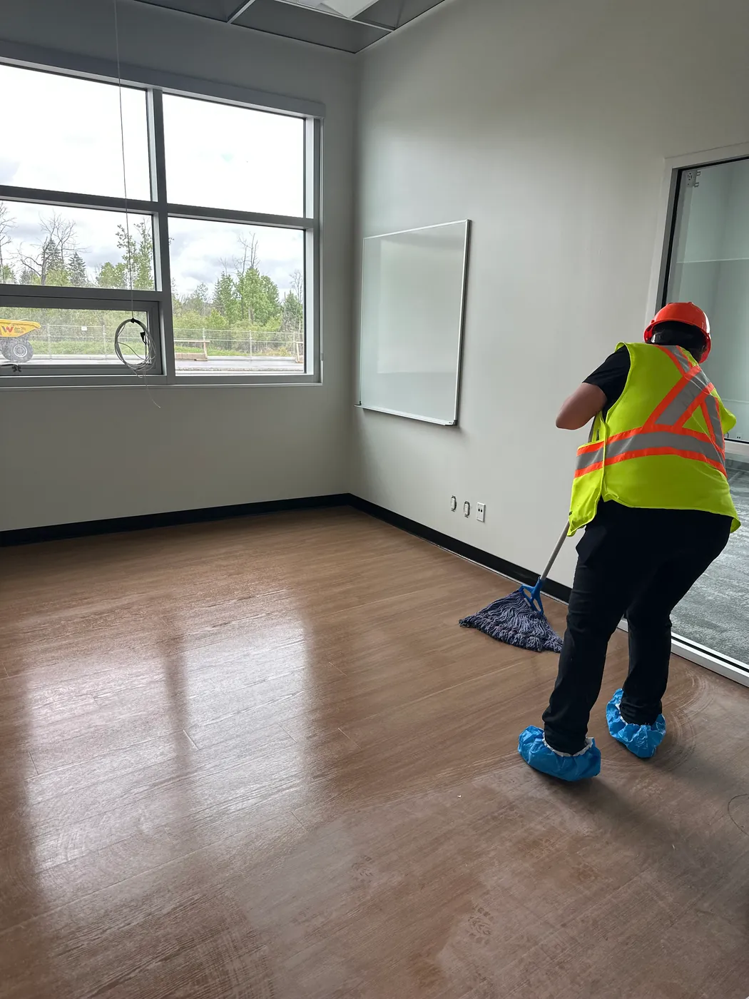 Kanians technician in a hi-vis vest and hard hat mopping the floor of a newly built office during post-construction cleaning
